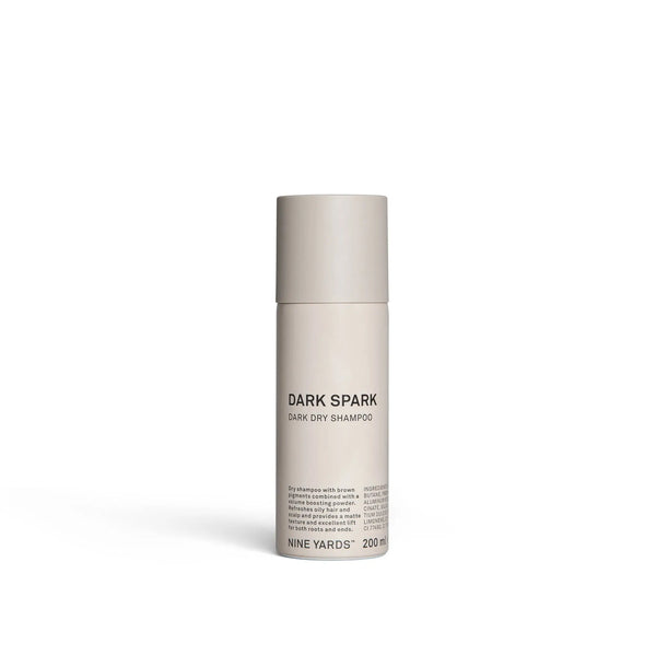 Smėlio spalvos cilindrinis buteliukas NINE YARDS Dark Spark Dark Dry Shampoo 200ml, paprastas minimalistinis dizainas ir derantis smėlio spalvos dangtelis. Produktas stovi baltame fone.